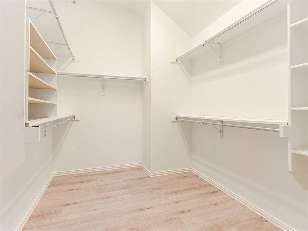 Walk-in closet featuring light wood-finish flooring and extensive built-in shelving units with integrated hanging rods