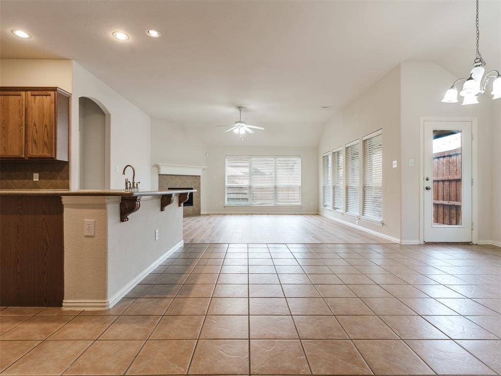 Open-concept space featuring tile flooring, wood-finish cabinetry, a peninsula with a stone countertop, a fireplace with a mantel, and wood-finish flooring