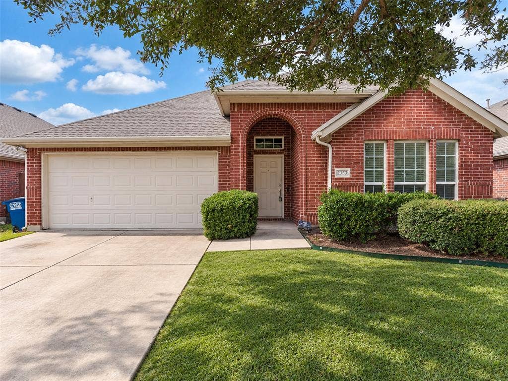 Red brick exterior featuring an arched entryway, a double-car garage, and a concrete driveway