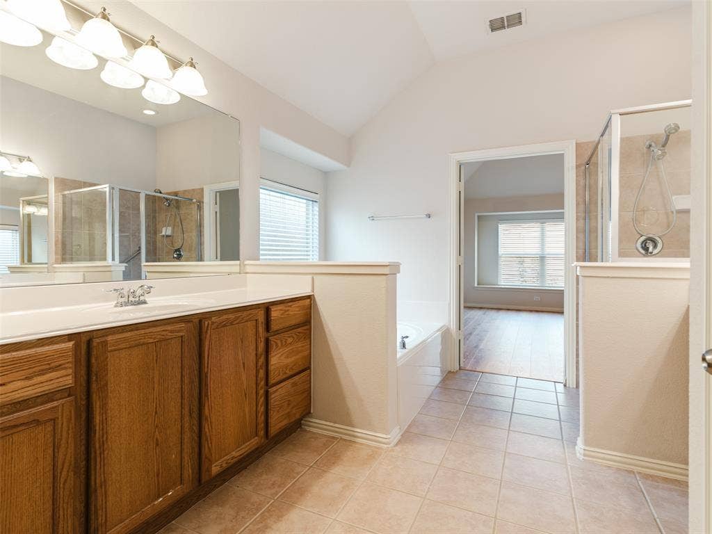 Bathroom featuring a wooden vanity, expansive wall-mounted mirror, ceramic tile flooring, deep soaking tub, and a glass-enclosed shower with tiled surround