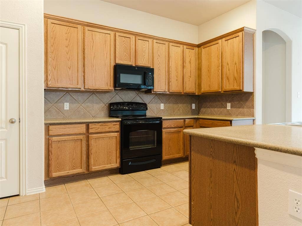 Kitchen featuring wood cabinetry, stone-finish countertops, black built-in oven and microwave, diagonal-set backsplash tile, and ceramic tile flooring