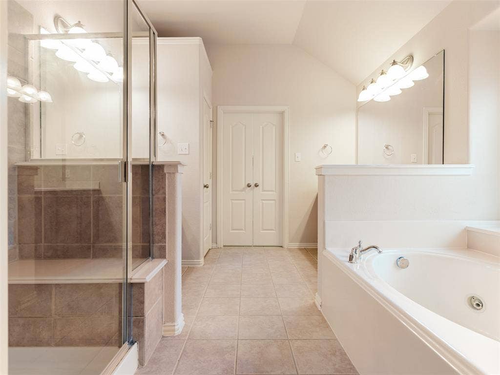 Bathroom featuring a tiled walk-in shower with a built-in bench, a jetted soaking tub, large wall-mounted mirrors, and multi-light fixtures