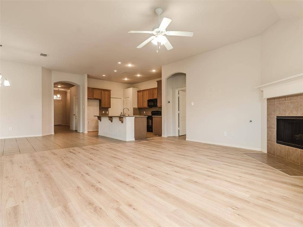 Open-concept interior featuring light wood-finish flooring, a neutral color palette, a tiled fireplace with a mantel, recessed lighting, and a kitchen island with built-in cabinetry