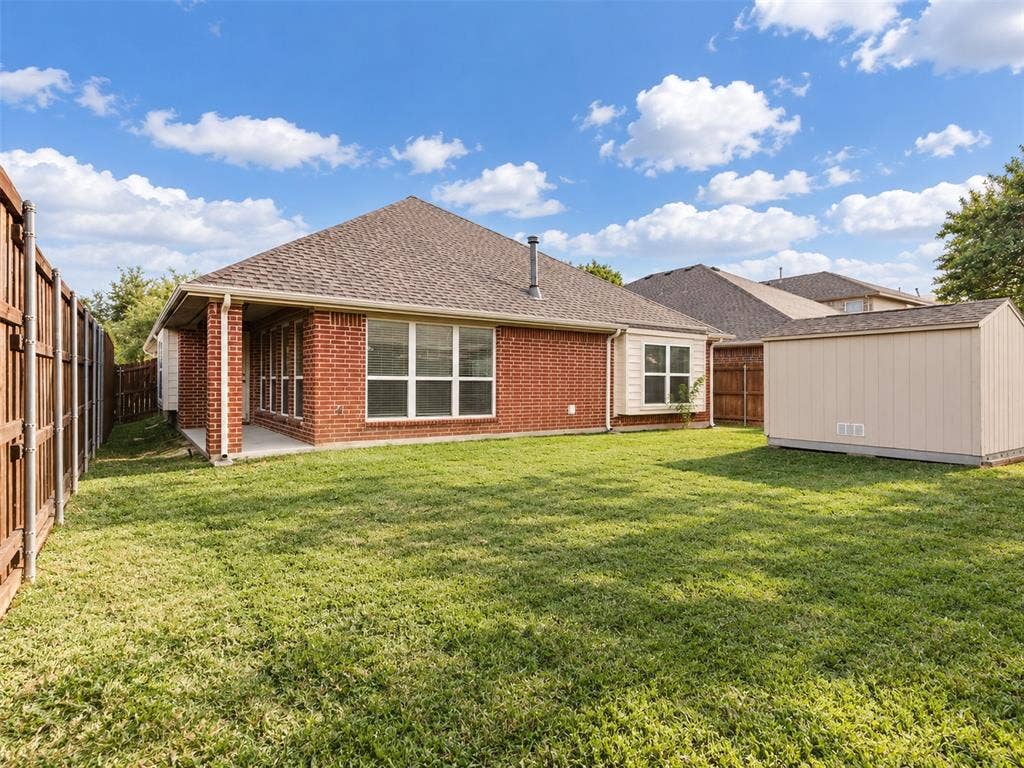 Backyard featuring a brick exterior, covered patio, manicured lawn, privacy fencing, and an exterior storage shed