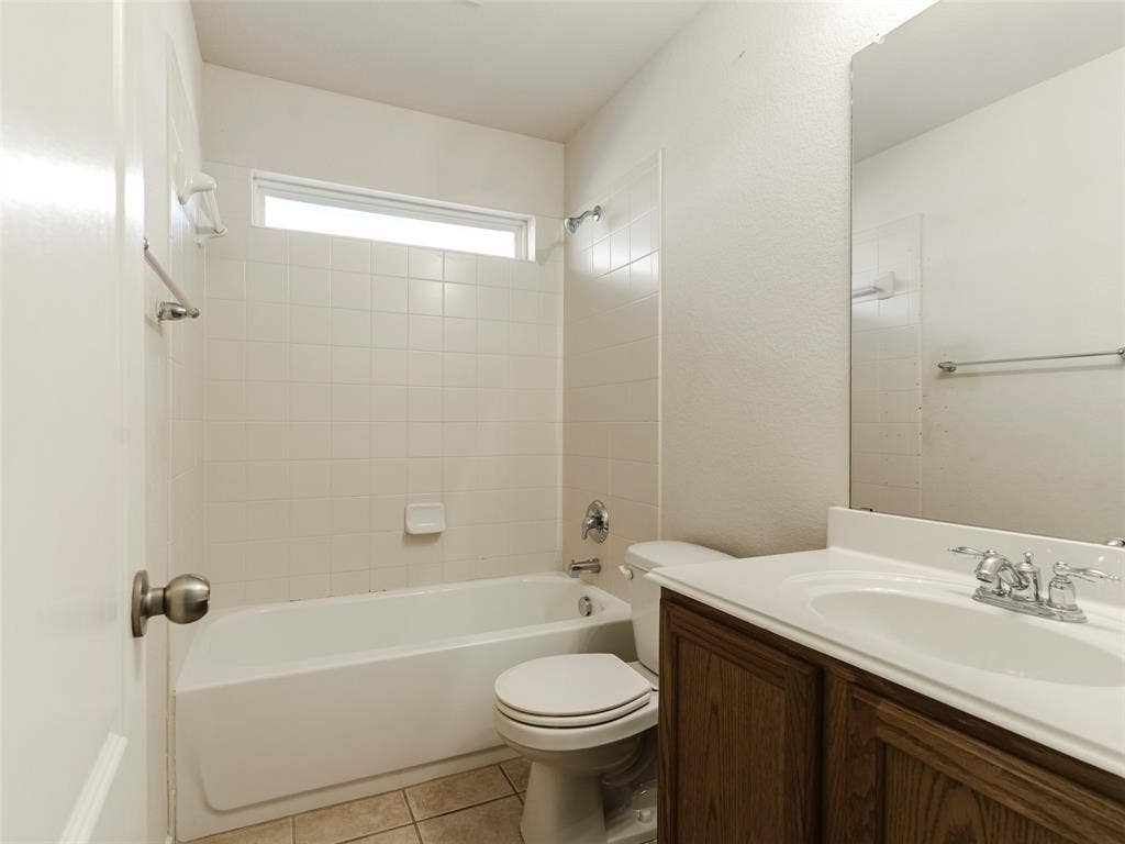 Full bathroom featuring a tub-shower combination with tile surround, high-set horizontal window, wood-finish vanity cabinet, integrated sink, and large wall-mounted mirror