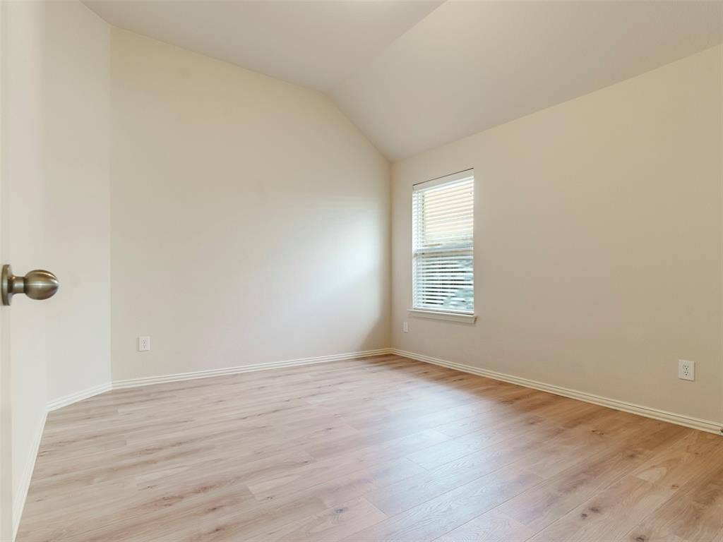 Neutral interior featuring wood-finish flooring, a vaulted ceiling, and a single window with horizontal blinds
