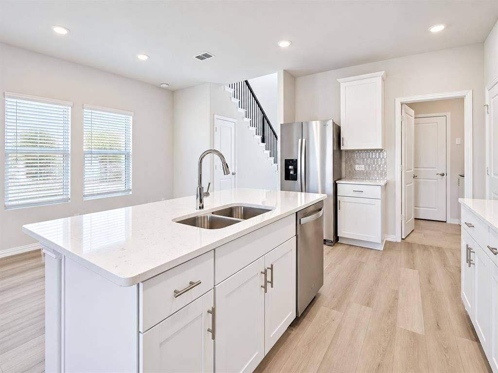 5204 Golden Trout Drive, Princeton, TX 75071 Modern kitchen featuring a large center island with dual sinks, white shaker cabinetry, stainless steel appliances, and wood-finish flooring
