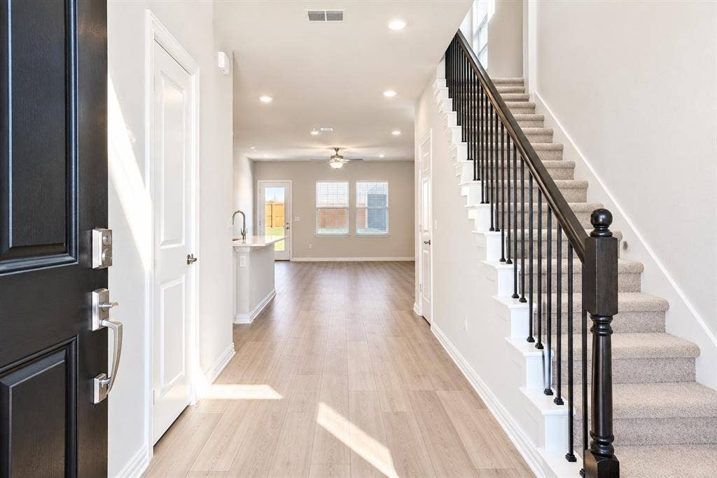 5204 Golden Trout Drive, Princeton, TX 75071 Wood-finish flooring, recessed lighting, carpeted staircase with dark wood newel post and black metal balusters, and a kitchen island with a single-basin sink