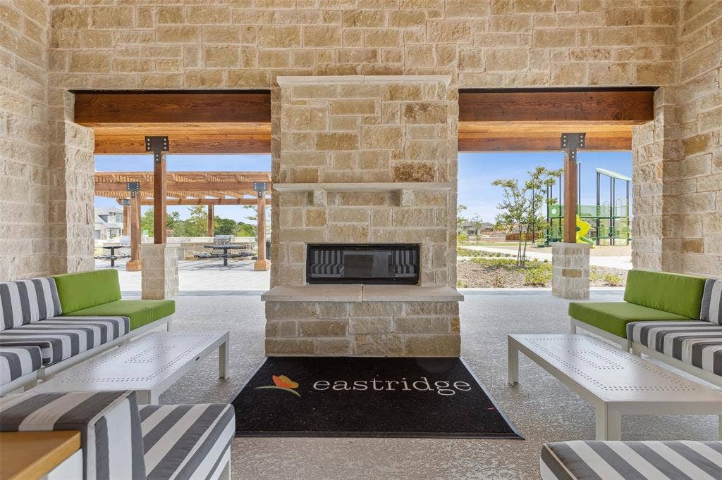 5204 Golden Trout Drive, Princeton, TX 75071 Stone-clad outdoor living space featuring a built-in fireplace, exposed wood beams, and a concrete floor