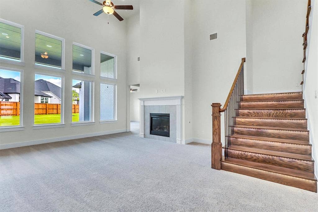 115 Cottonwood Court, Murphy, TX 75094 Two-story living area featuring a fireplace with a mantel, a ceiling fan, a carpeted floor, and a wood staircase with metal balusters