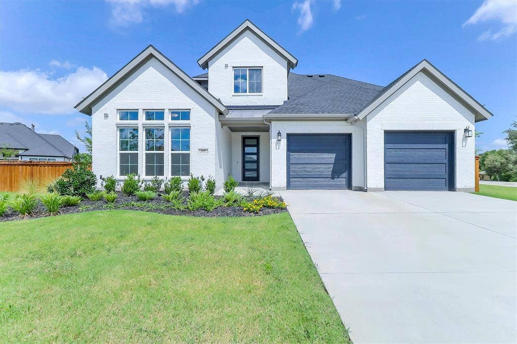 115 Cottonwood Court, Murphy, TX 75094 White brick exterior with a dark gray shingle roof, featuring a two-car garage with dark blue doors, a prominent front gable, and a concrete driveway