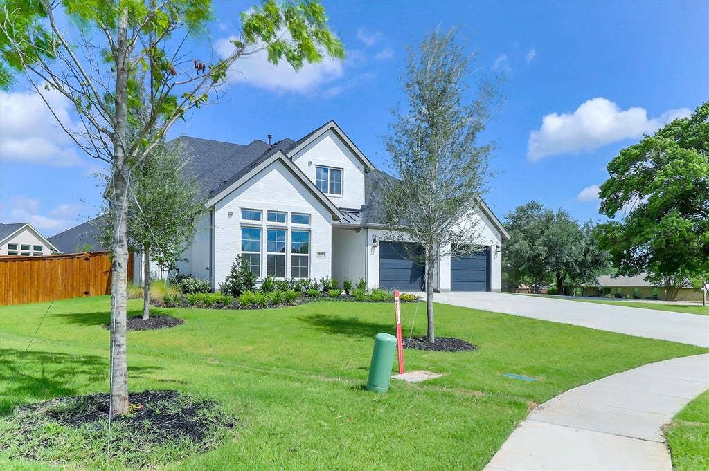 115 Cottonwood Court, Murphy, TX 75094 White brick exterior with dark gray roof, multiple gables, attached two-car garage, concrete driveway, and a front yard with mature landscaping