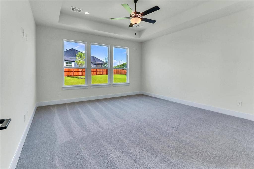 115 Cottonwood Court, Murphy, TX 75094 Spacious room featuring light gray carpeting, tray ceiling, ceiling fan with integrated lighting, and three large windows