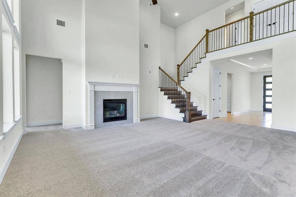 115 Cottonwood Court, Murphy, TX 75094 Two-story living area featuring a fireplace with a light-toned surround, a grand staircase with dark wood treads and wrought iron balusters, and a carpeted floor
