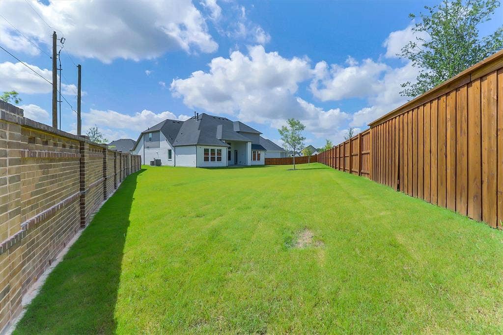 115 Cottonwood Court, Murphy, TX 75094 Expansive green lawn, brick perimeter wall, and a wood privacy fence enclose the rear of the property