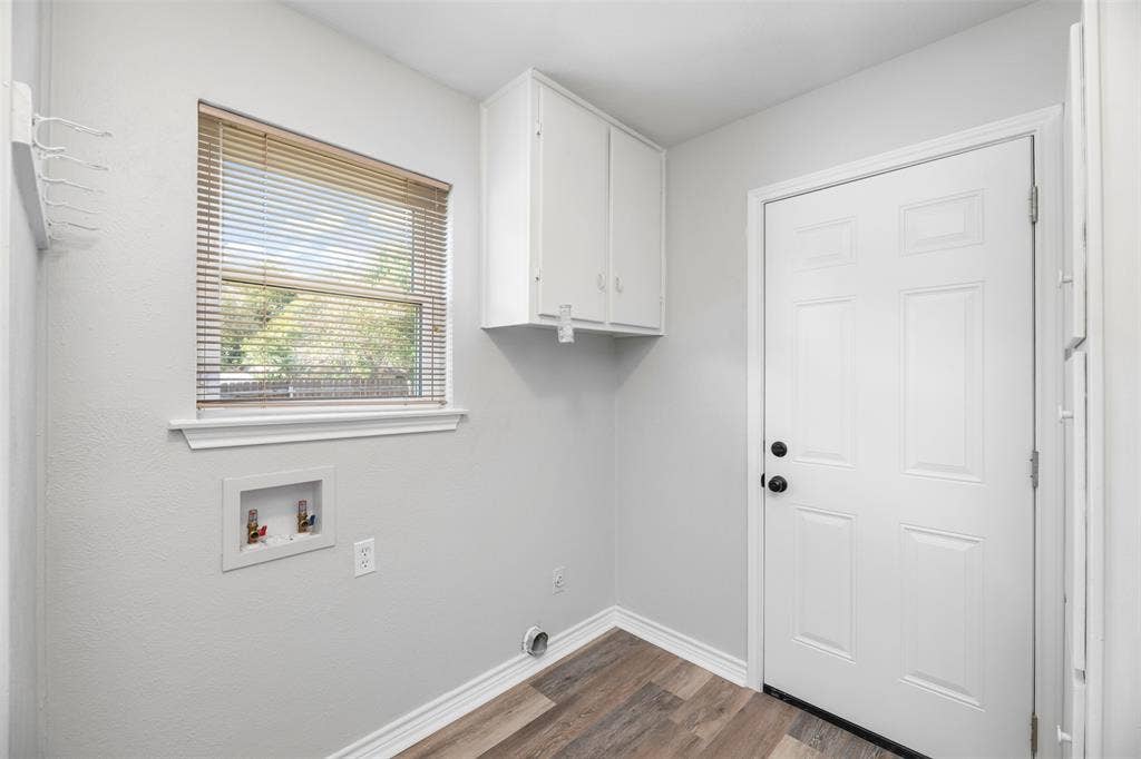 Utility room with wood-finish flooring, white paneled door, and built-in white cabinetry