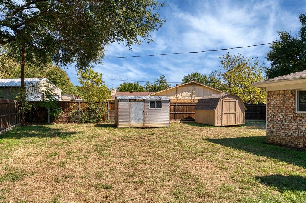 Expansive backyard with a wooden fence boundary, two storage sheds, and mature trees