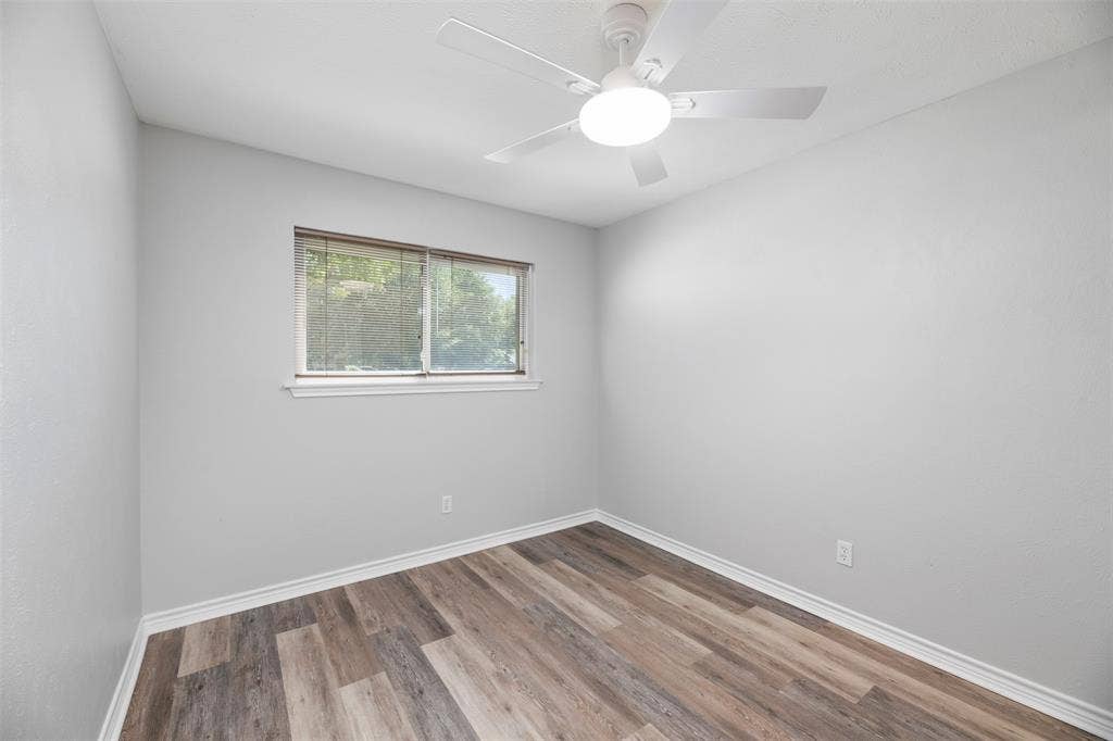 Wood-finish flooring, white ceiling fan with integrated lighting, and a window with a white frame