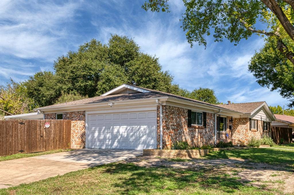 Brick exterior, attached garage, composition shingle roof, wood privacy fence, and mature landscaping