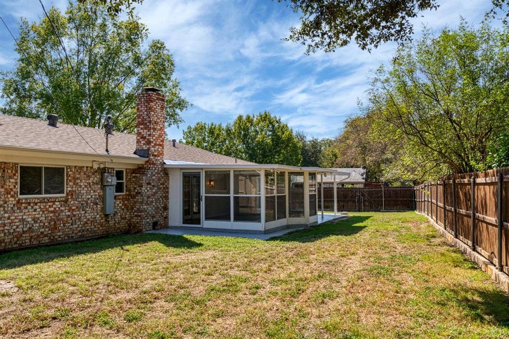 Brick exterior with a prominent brick chimney, screened-in enclosure, concrete patio, and wood privacy fencing