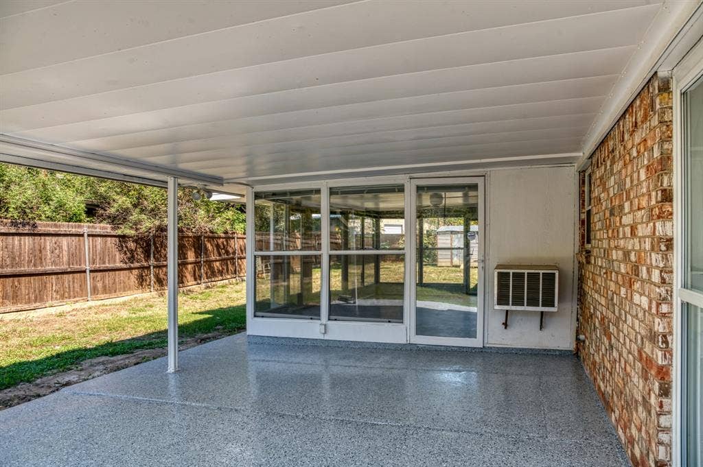 Covered patio with a speckled concrete finish, offering direct access to an enclosed sunroom through a glass-paneled door