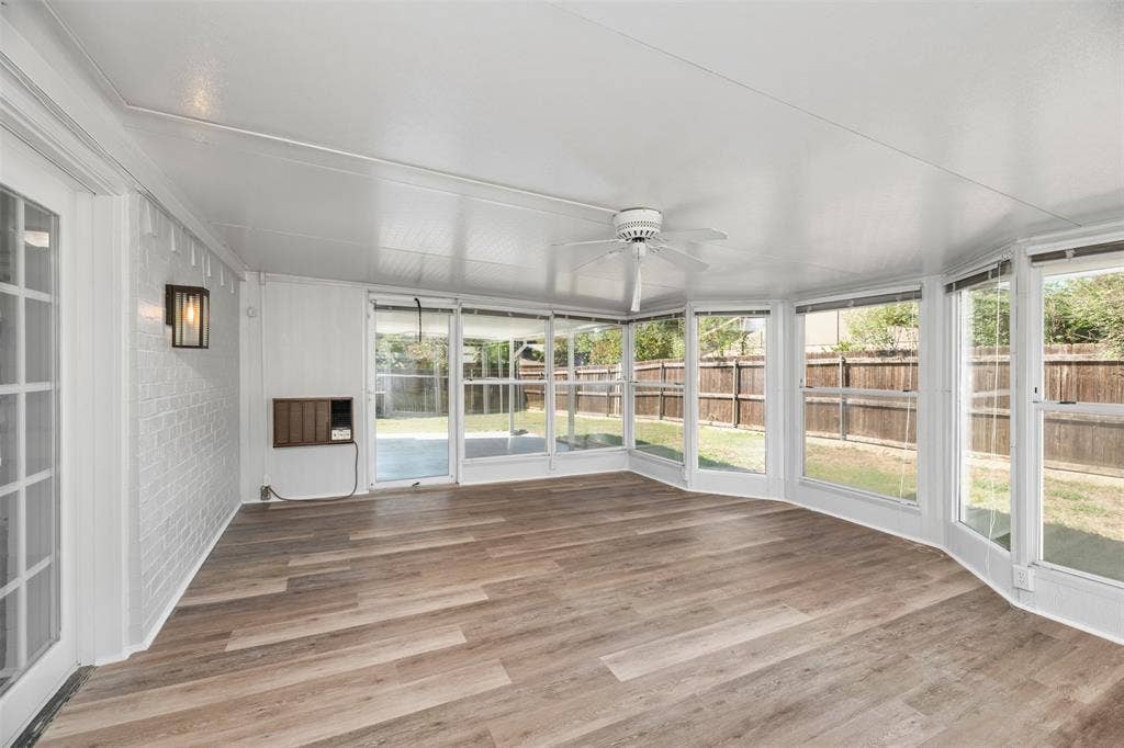 Expansive sunroom featuring wood-finish flooring, a ceiling fan, white paneled walls, and abundant natural light from multiple windows