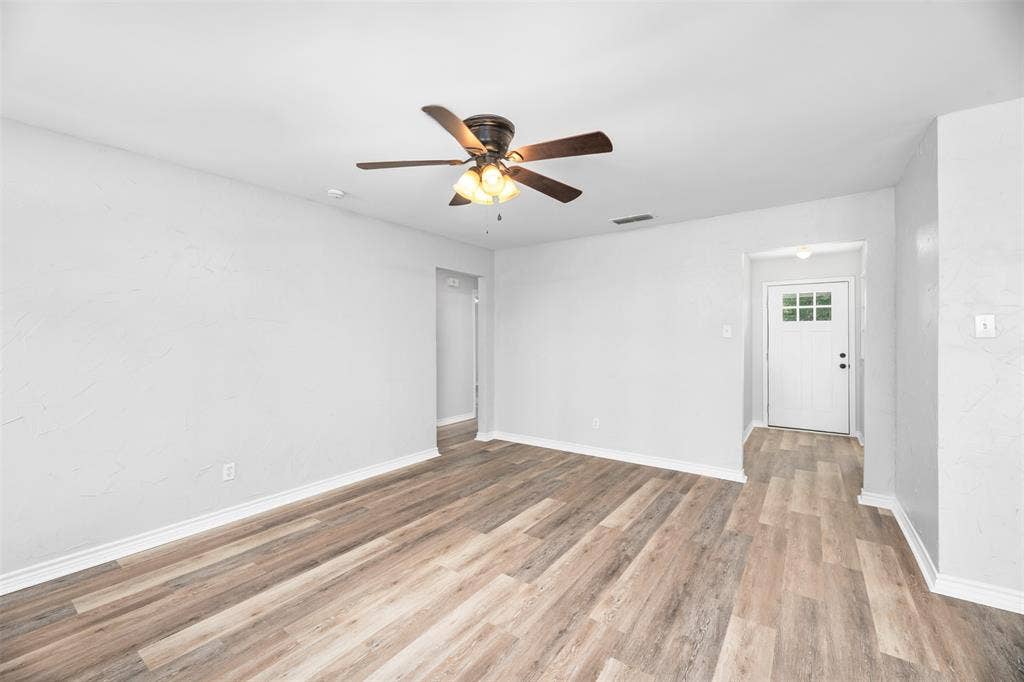 Wood-finish flooring, ceiling fan with integrated lighting, white walls, and a white paneled door with window inserts