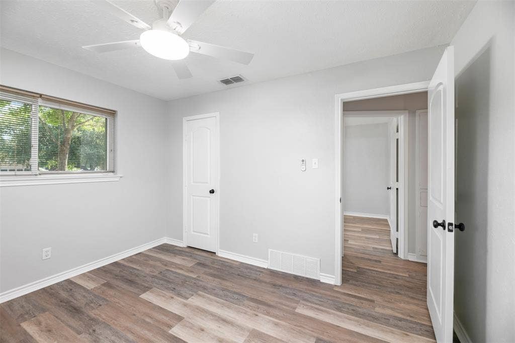 Wood-finish flooring, light gray wall tones, a ceiling fan with integrated lighting, and a window with blinds