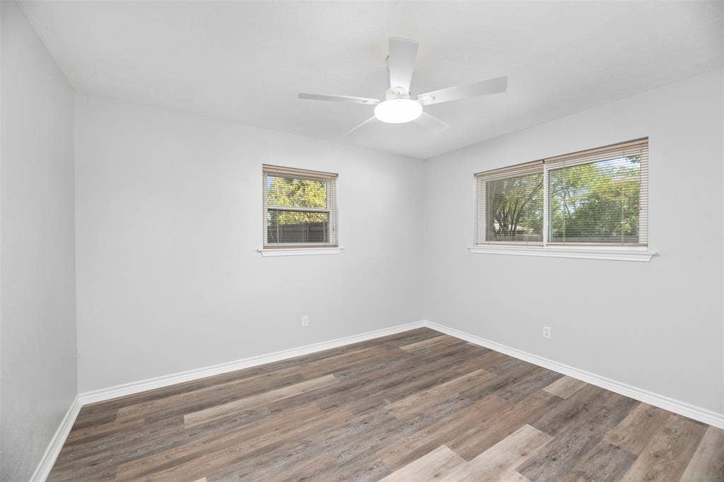 Wood-finish flooring, white walls, two windows, and a ceiling fan with integrated lighting