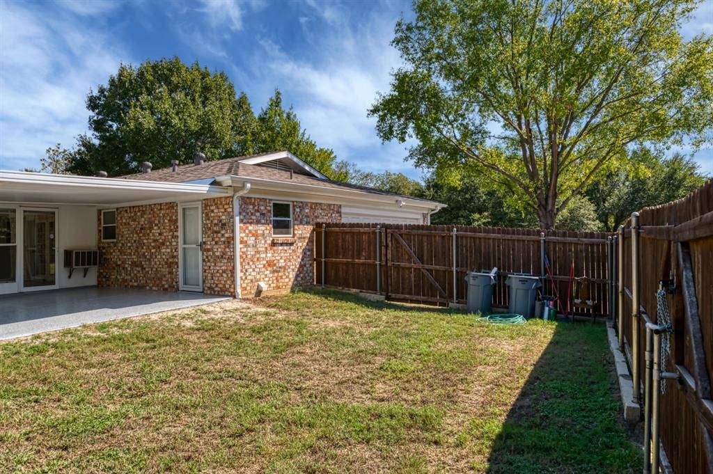 Expansive outdoor space featuring a covered patio, a full privacy fence, and mature trees