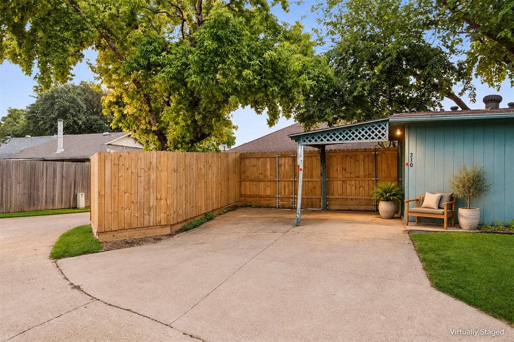 Expansive concrete driveway with a wooden privacy fence, mature trees, and a covered carport with lattice detailing