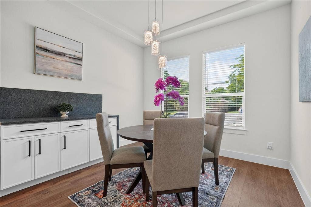 3210 Carpenter Avenue, Dallas, TX 75215 Wood-finish flooring, white cabinetry with black hardware, dark stone countertop with matching backsplash, and a contemporary chandelier