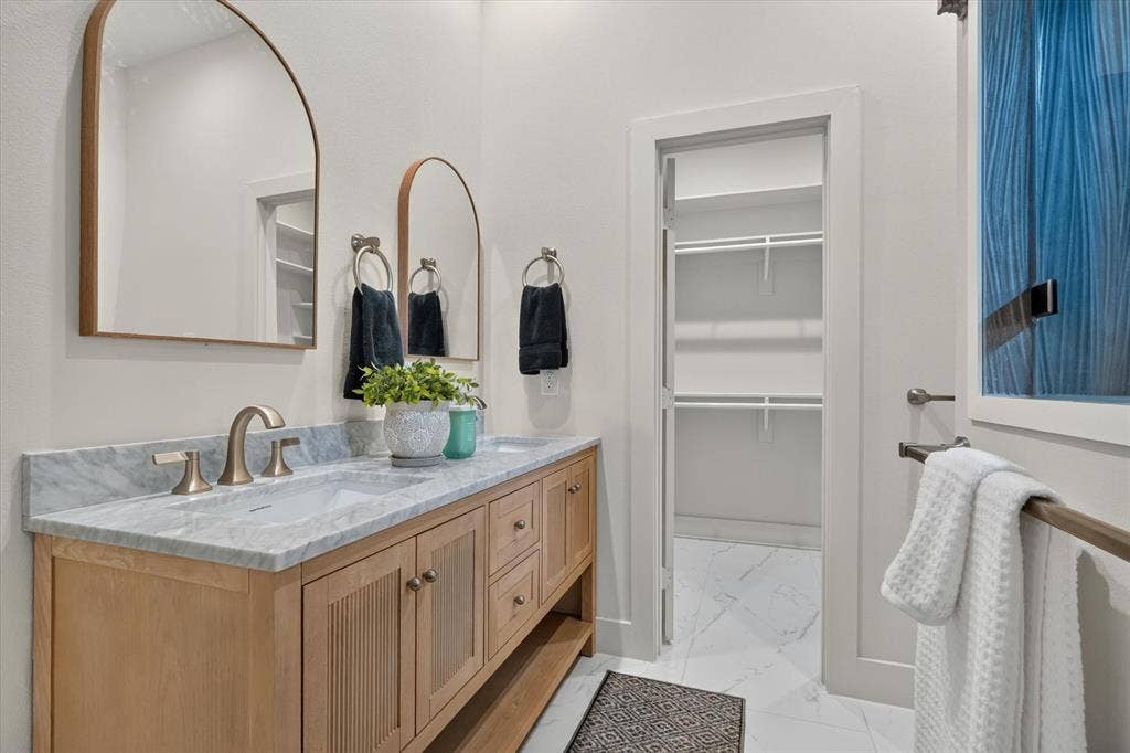 3210 Carpenter Avenue, Dallas, TX 75215 Double vanity with undermount sinks and light wood-finish cabinetry, arched mirrors, and a walk-in closet with built-in shelving