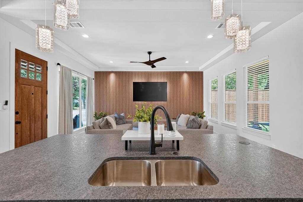 3210 Carpenter Avenue, Dallas, TX 75215 Dual basin stainless steel sink, dark textured countertop, wood-finish accent wall, ceiling fan, and multiple pendant light fixtures