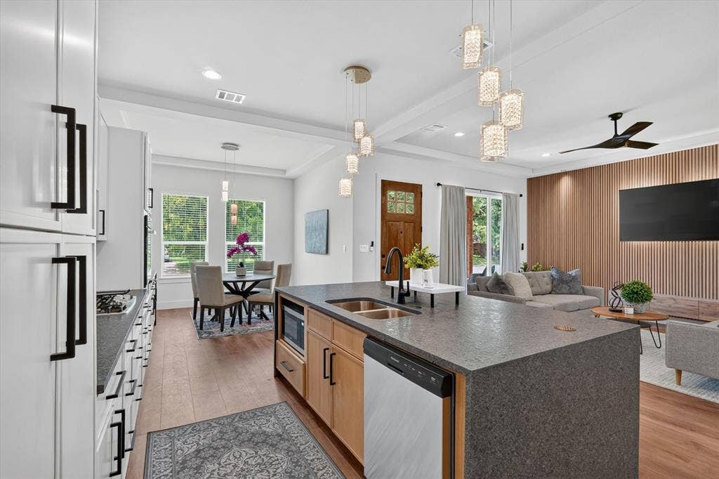 3210 Carpenter Avenue, Dallas, TX 75215 Spacious kitchen island with an integrated sink and dishwasher, white cabinetry with black hardware, wood-finish flooring, and a dining area with pendant lighting
