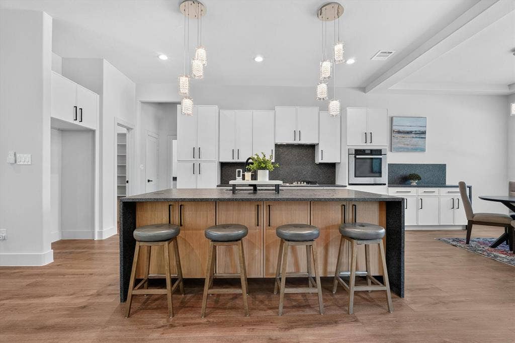 3210 Carpenter Avenue, Dallas, TX 75215 Kitchen featuring a two-tone island with dark countertops, white cabinetry with dark hardware, a built-in oven, and wood-finish flooring