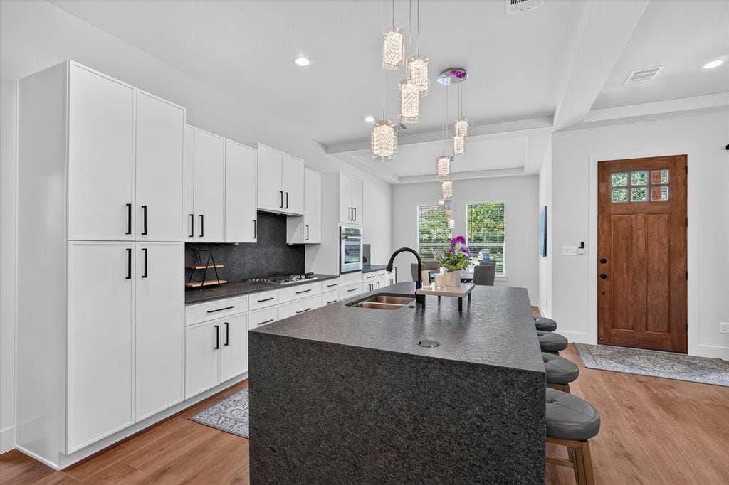 3210 Carpenter Avenue, Dallas, TX 75215 Gourmet kitchen featuring white cabinetry, a large center island with integrated sink, black stone countertops, and wood-finish flooring