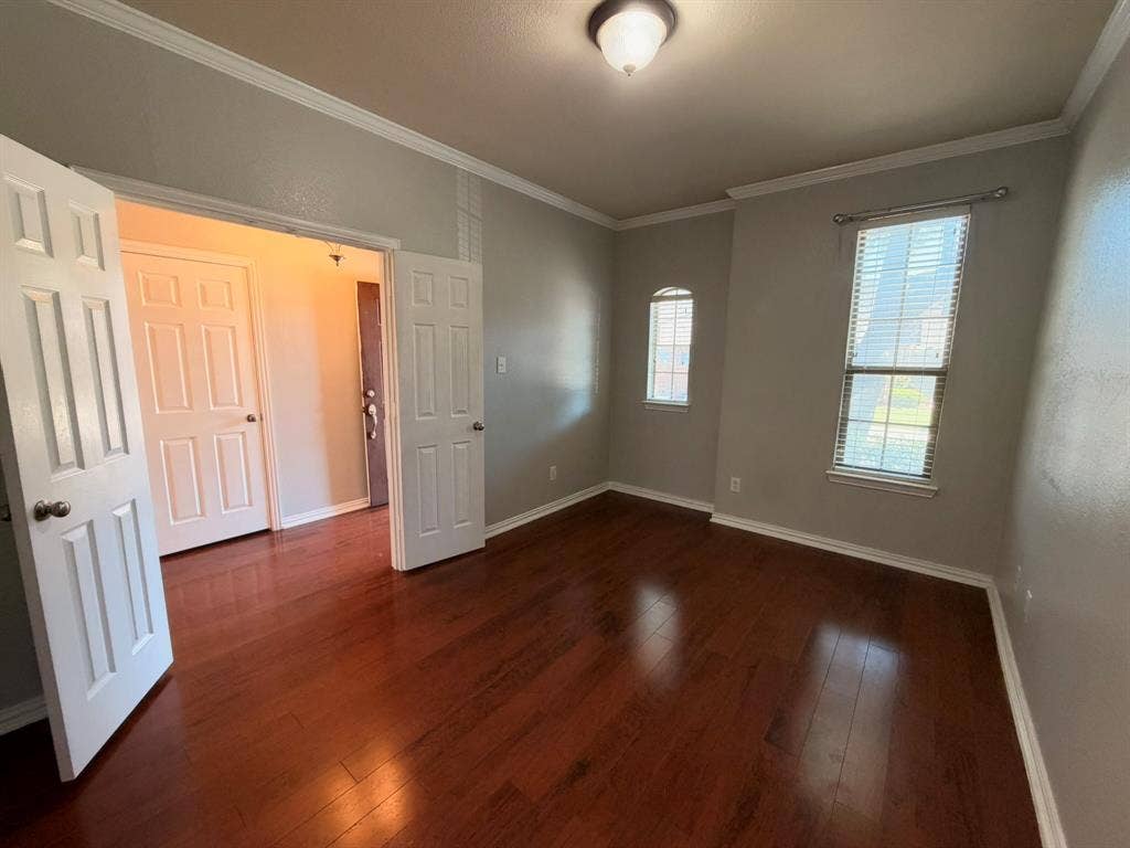 5016 Rushden Road, McKinney, TX 75070 Rich wood-finish flooring, two large windows with blinds, a compact arched window, a ceiling-mounted light fixture, and crown molding