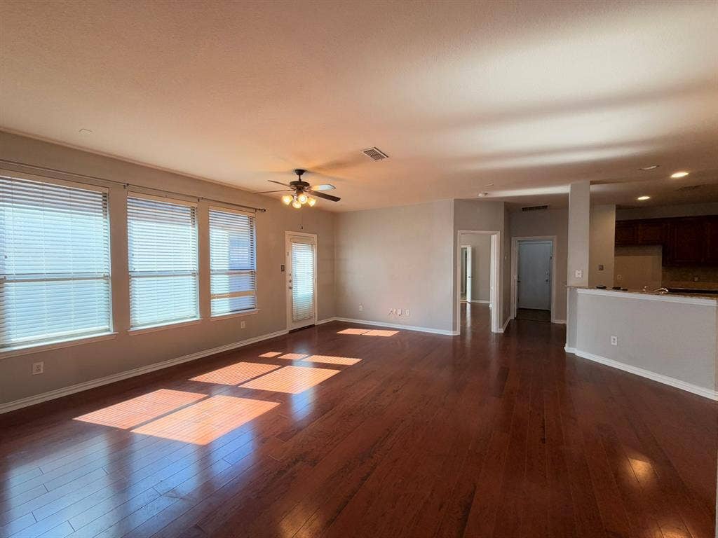 5016 Rushden Road, McKinney, TX 75070 Hardwood flooring, multiple windows with blinds, ceiling fan with integrated lighting, a glass-paneled door, and a partial view of kitchen cabinetry