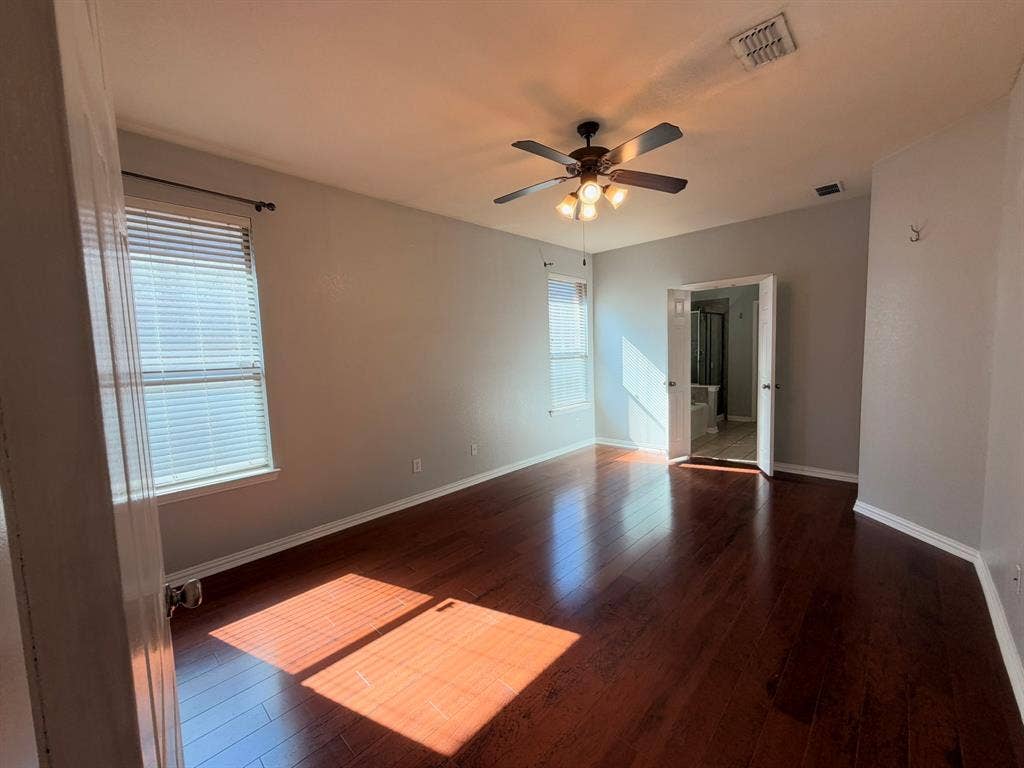 5016 Rushden Road, McKinney, TX 75070 Dark wood-finish flooring, two window openings with blinds, ceiling fan with integrated lighting, and an open doorway revealing a bathtub