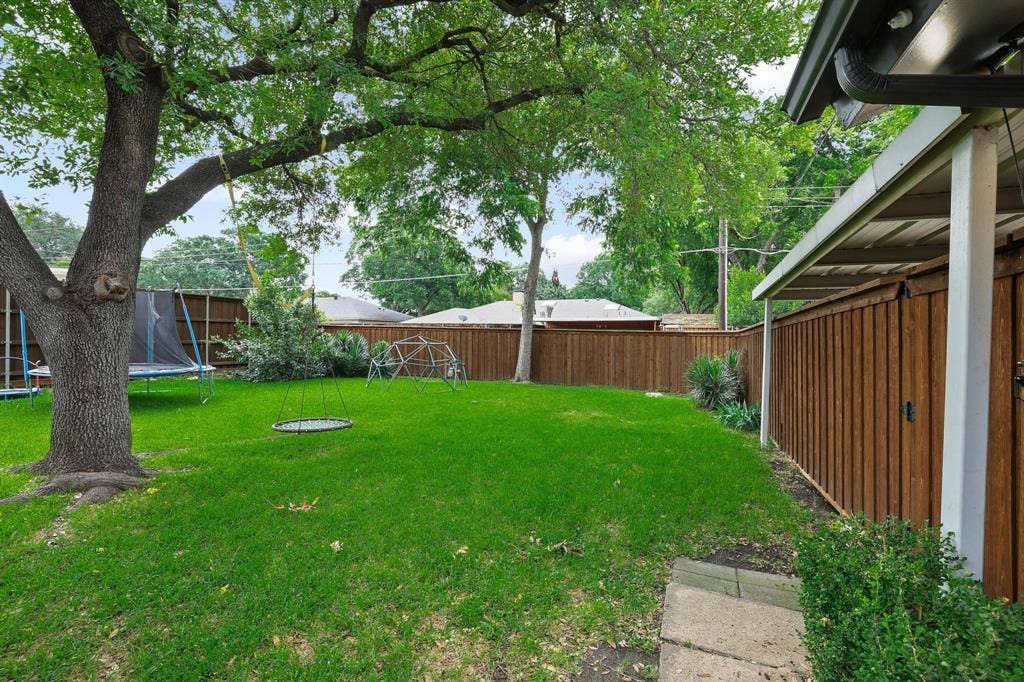 7668 La Cosa Drive, Dallas, TX 75248 Expansive backyard featuring a mature tree, concrete stepping stones, and a full privacy fence