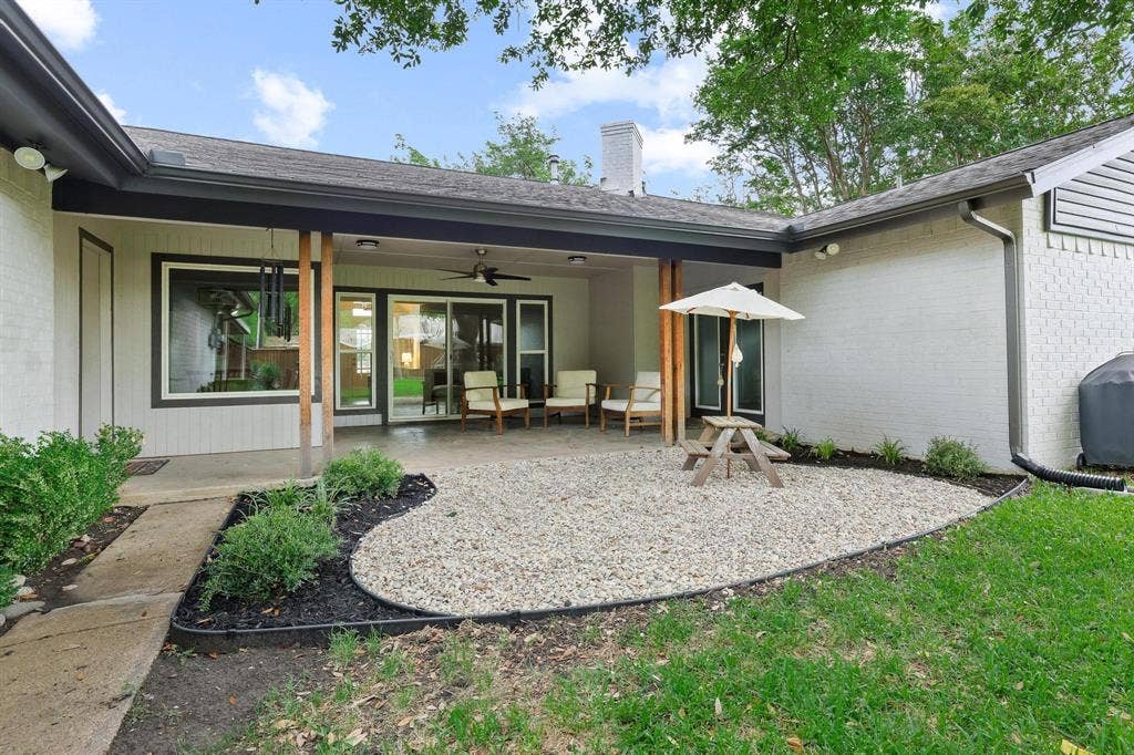 7668 La Cosa Drive, Dallas, TX 75248 Covered patio with a concrete slab, sliding glass doors, white brick exterior, and a gravel-filled landscaping bed