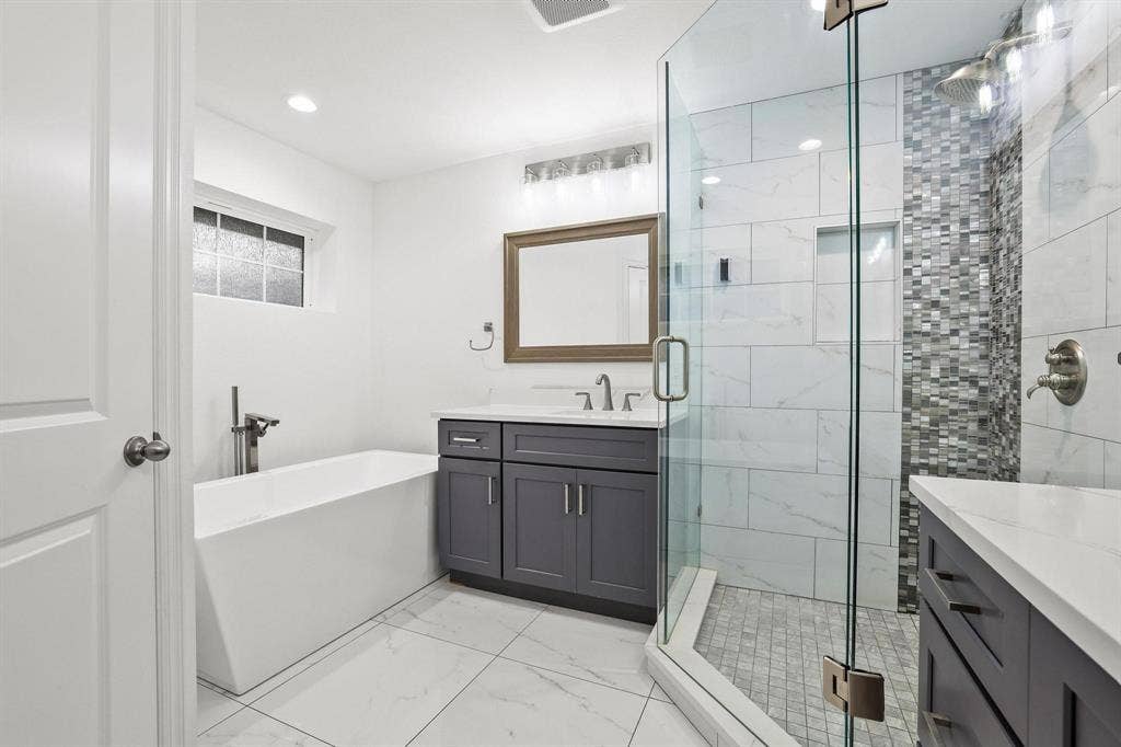 7668 La Cosa Drive, Dallas, TX 75248 Freestanding soaking tub with floor-mounted fixture, glass-enclosed shower with mosaic tile accent, dual vanities with white countertops, and recessed lighting