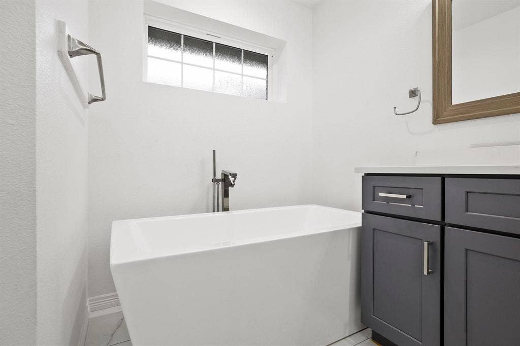 7668 La Cosa Drive, Dallas, TX 75248 Freestanding soaking tub with a floor-mounted faucet, dark gray vanity cabinetry, and a framed mirror