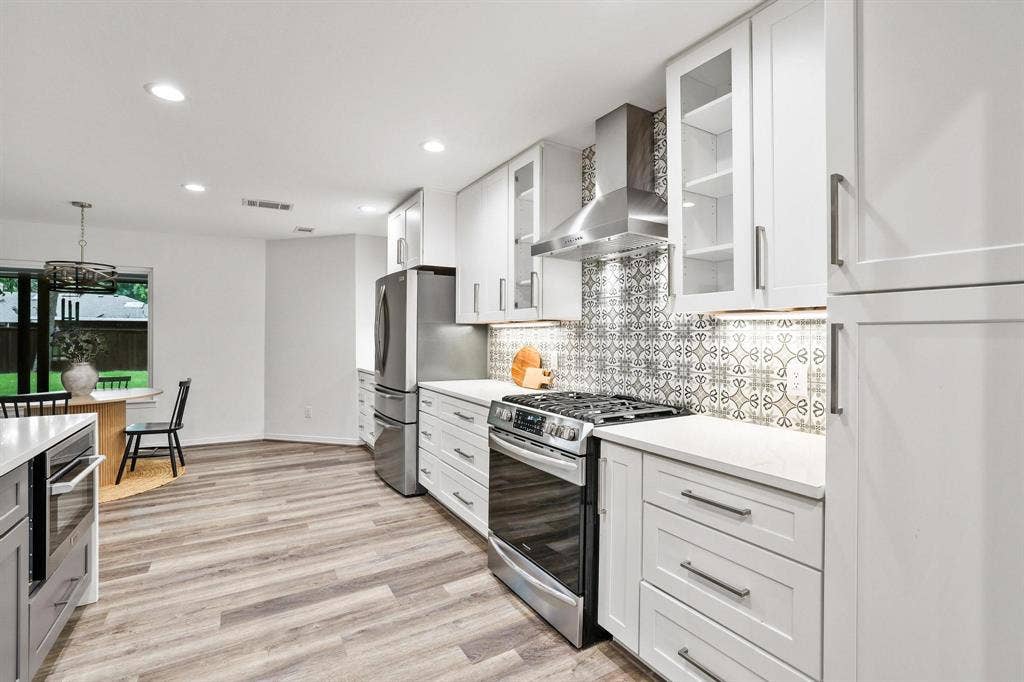 7668 La Cosa Drive, Dallas, TX 75248 Modern kitchen featuring white shaker cabinetry, patterned tile backsplash, stainless steel appliances, and wood-finish flooring