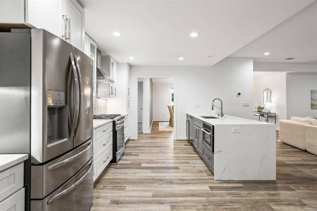 7668 La Cosa Drive, Dallas, TX 75248 Stainless steel appliances, white cabinetry, wood-finish flooring, recessed lighting, and a kitchen island with sink