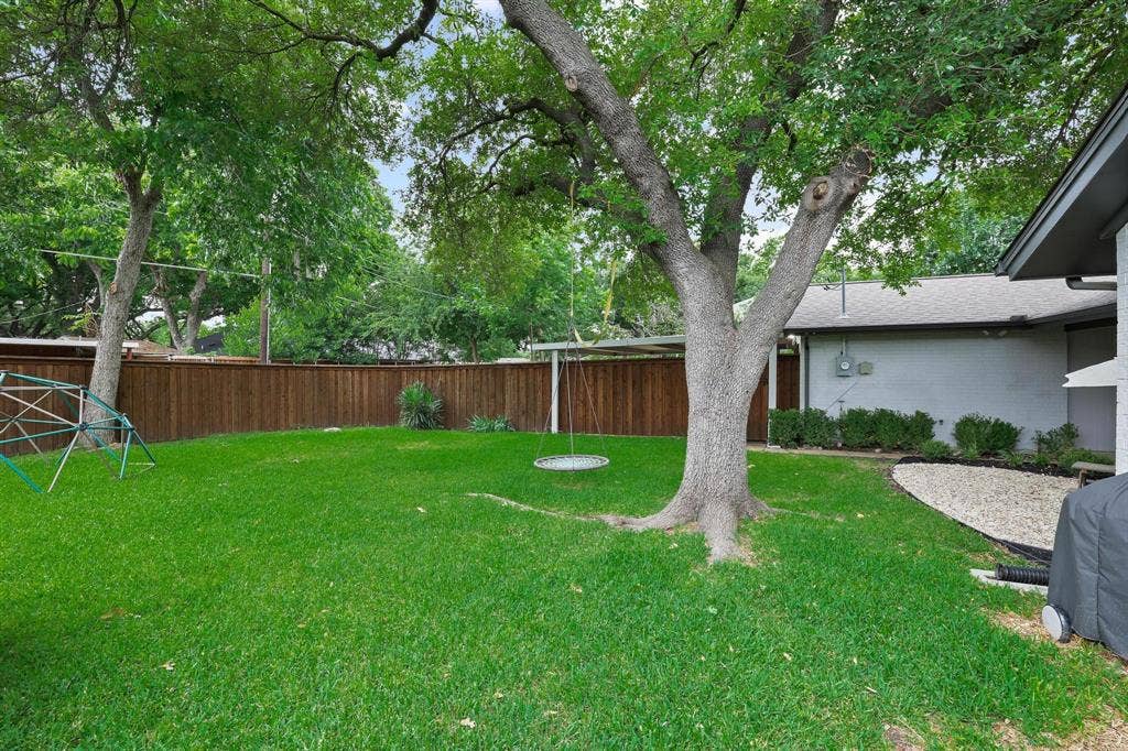 7668 La Cosa Drive, Dallas, TX 75248 Expansive backyard featuring a manicured lawn, mature trees, wood fence, and gravel landscaping
