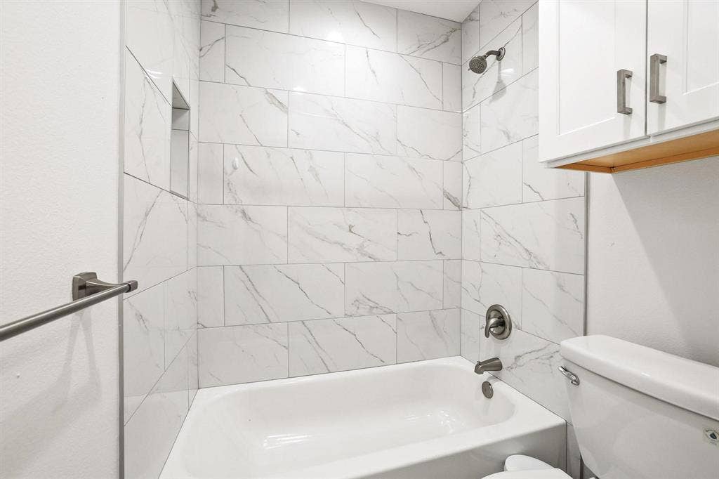 7668 La Cosa Drive, Dallas, TX 75248 Bathtub with full-height subway tile surround, recessed shower niche, and brushed nickel fixtures