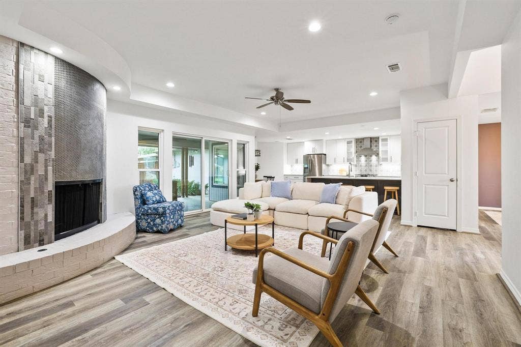 7668 La Cosa Drive, Dallas, TX 75248 Spacious living area featuring wood-finish flooring, a curved fireplace with brick and tile accents, and recessed lighting