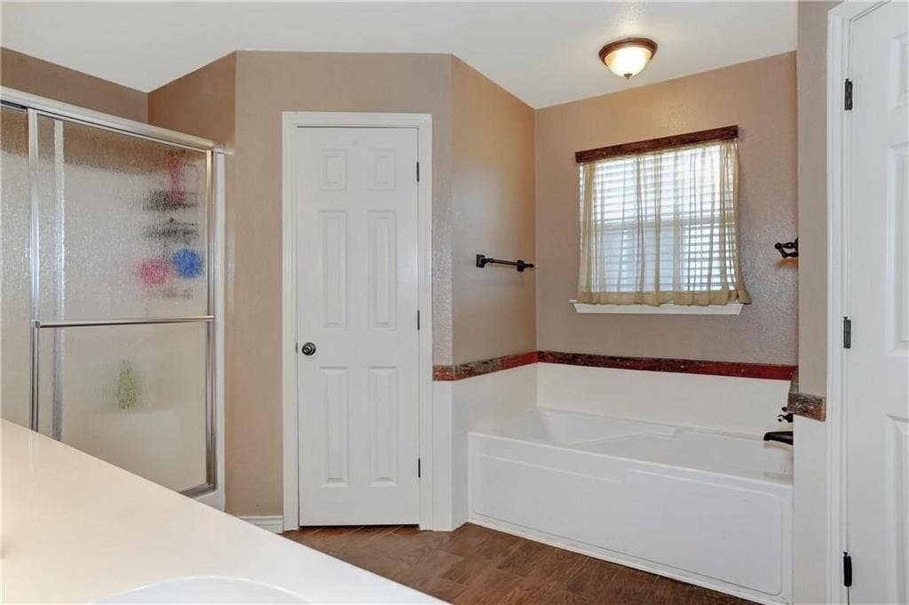 12875 Westover Lane, Anna, TX 75409 Shower enclosure with sliding glass door, white bathtub, wood-finish flooring, and a white six-panel door